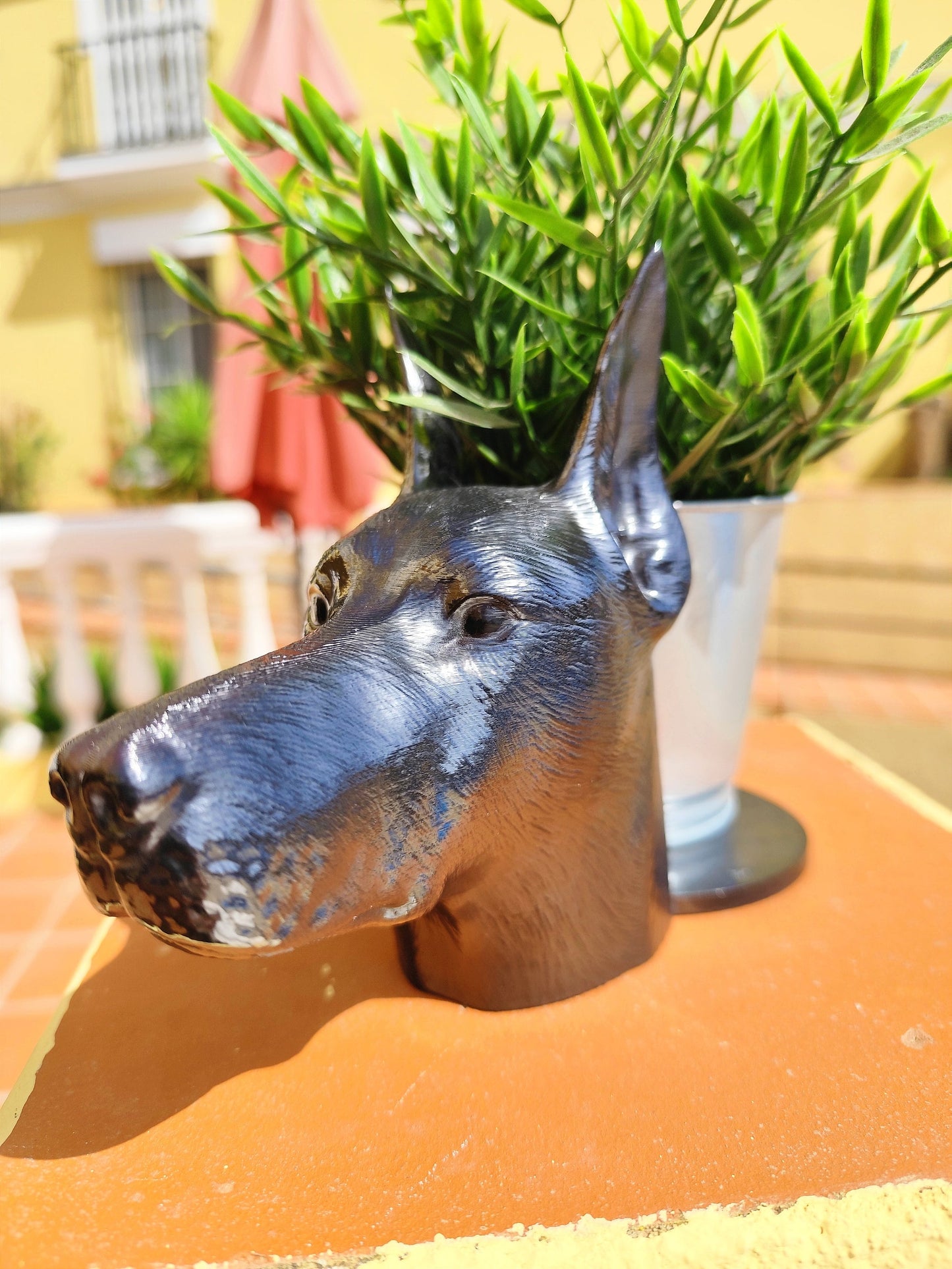 Side view of a hand-painted Doberman planter with metallic gold and silver accents, showcasing the Doberman&#39;s sleek profile. A green plant is placed inside the planter, creating a stylish décor piece for indoor or outdoor use.