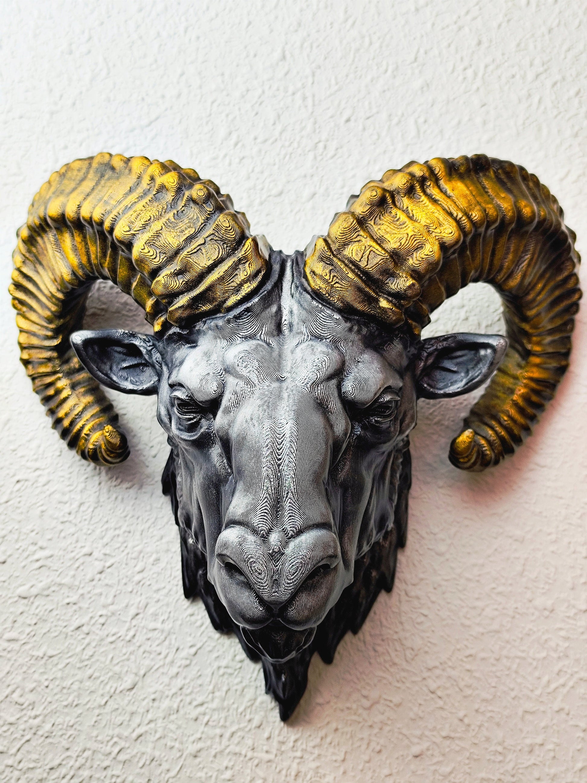 Side view of a hand-painted ram head wall mount, showcasing the intricate metallic gold and silver details on the horns and realistic facial structure. The sculpture is mounted on a white wall, highlighting its striking design