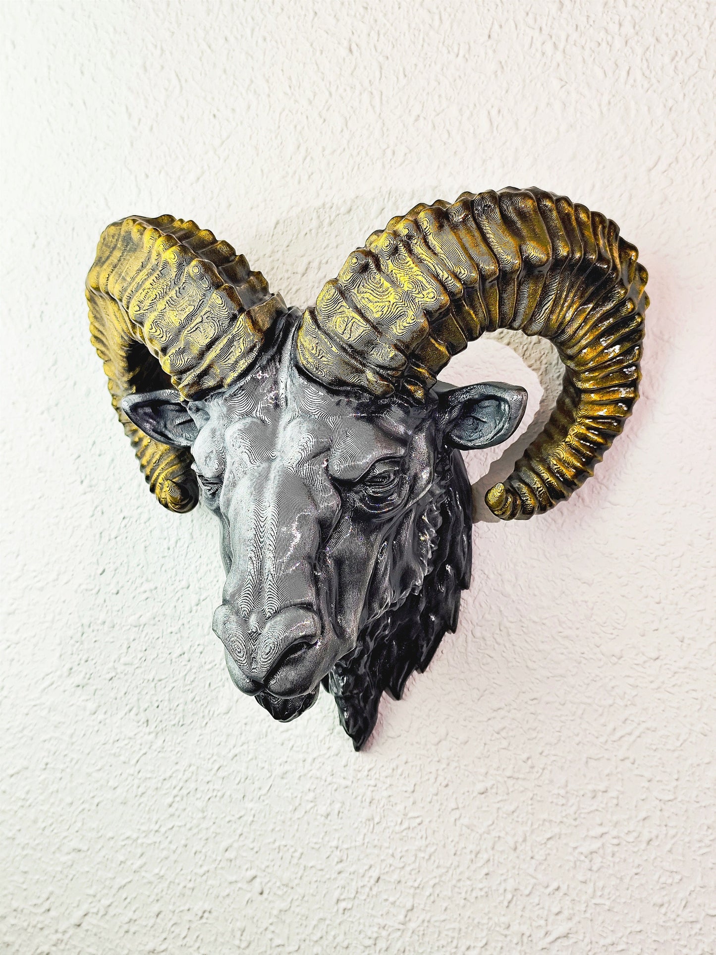 Side view of a hand-painted ram head wall mount, showcasing the intricate metallic gold and silver details on the horns and realistic facial structure. The sculpture is mounted on a white wall, highlighting its striking design