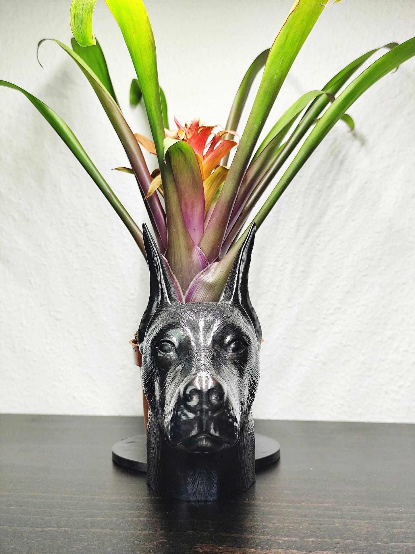 Close-up of a hand-painted Doberman planter featuring metallic gold and silver detailing, with a small green plant in the background. The planter captures the lifelike features of a Doberman&#39;s head with intricate details