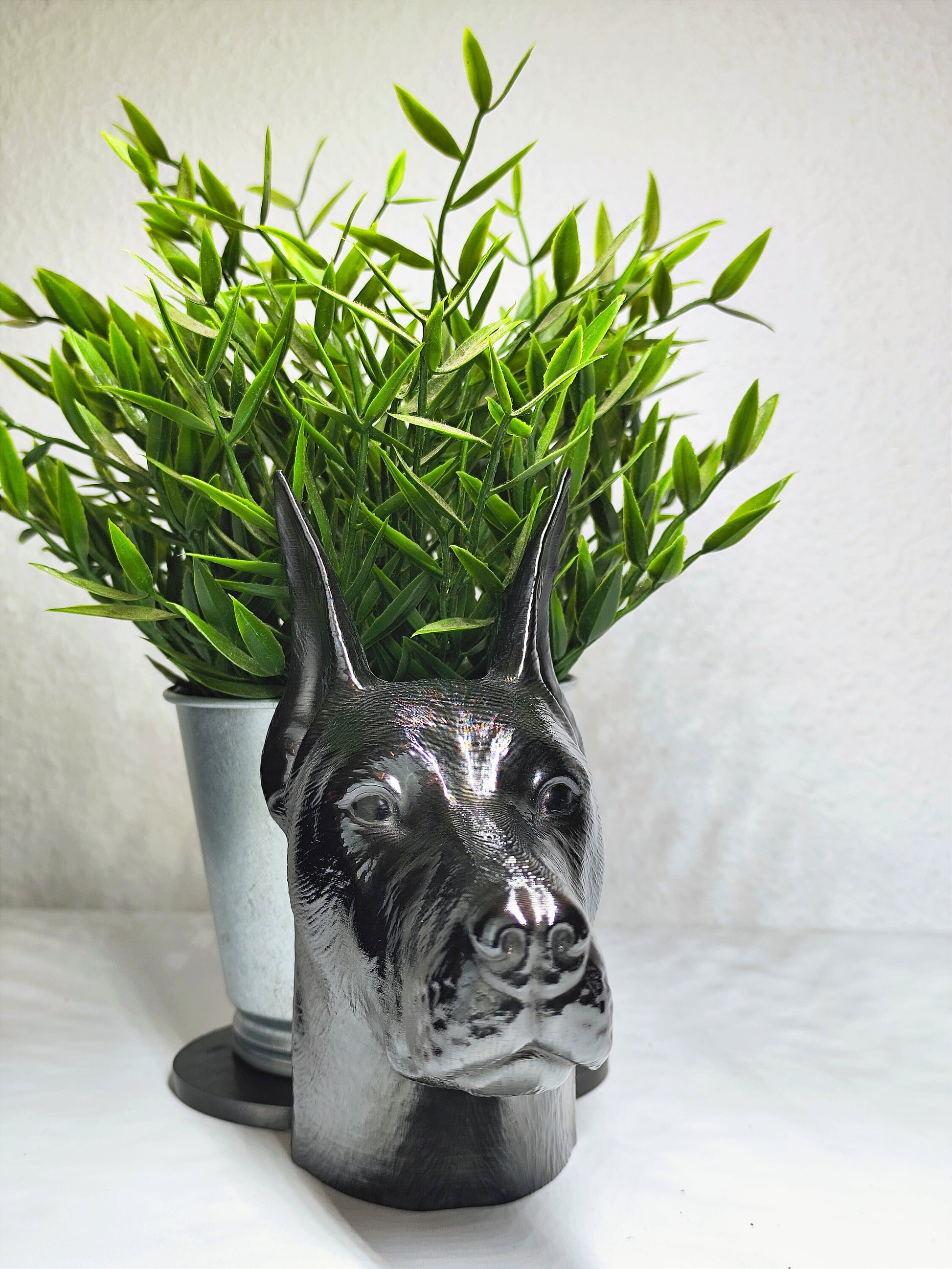 Close-up of a hand-painted Doberman planter featuring metallic gold and silver detailing, with a small green plant in the background. The planter captures the lifelike features of a Doberman&#39;s head with intricate details