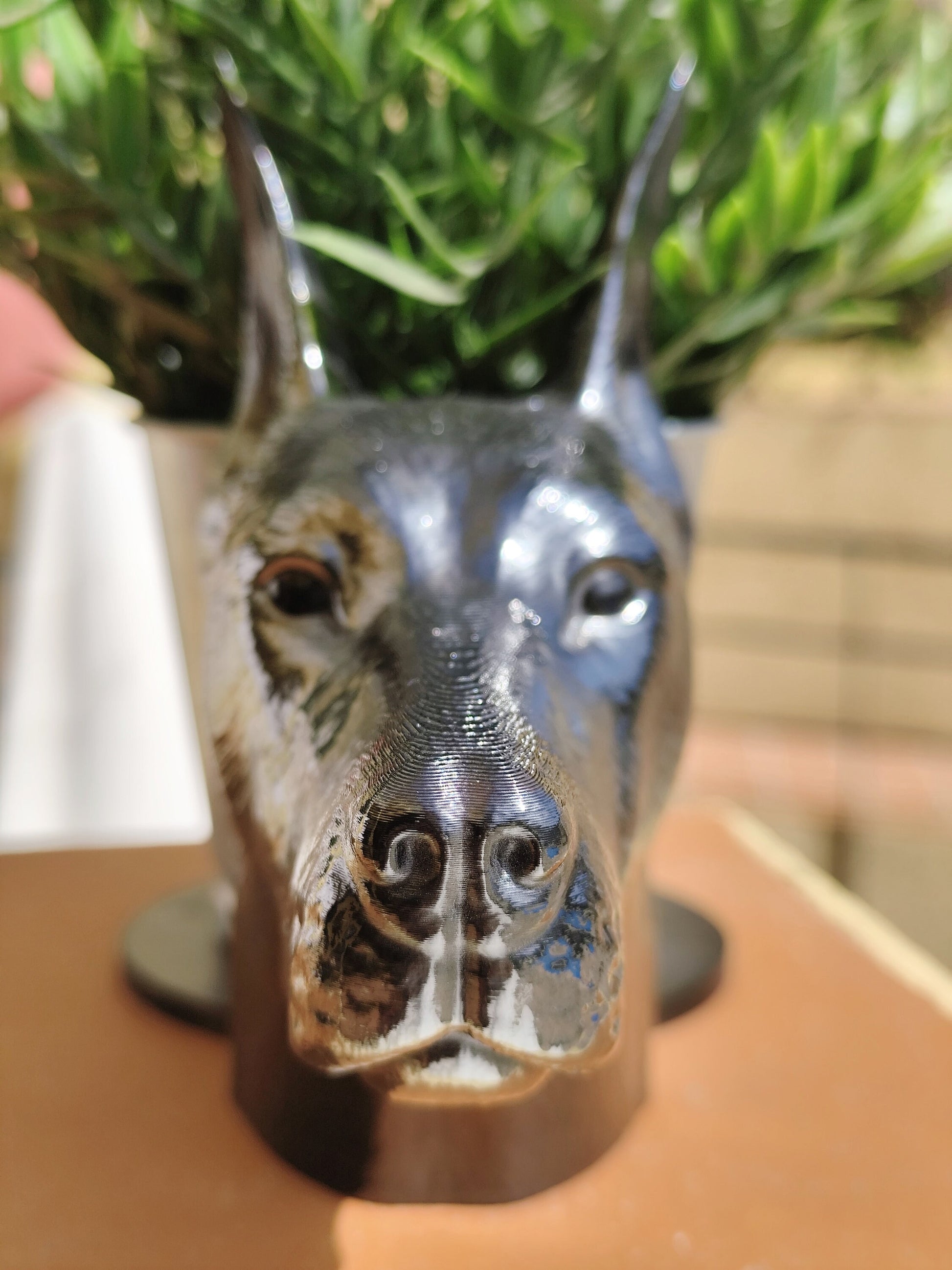 Side view of a hand-painted Doberman planter with metallic gold and silver accents, showcasing the Doberman&#39;s sleek profile. A green plant is placed inside the planter, creating a stylish décor piece for indoor or outdoor use.