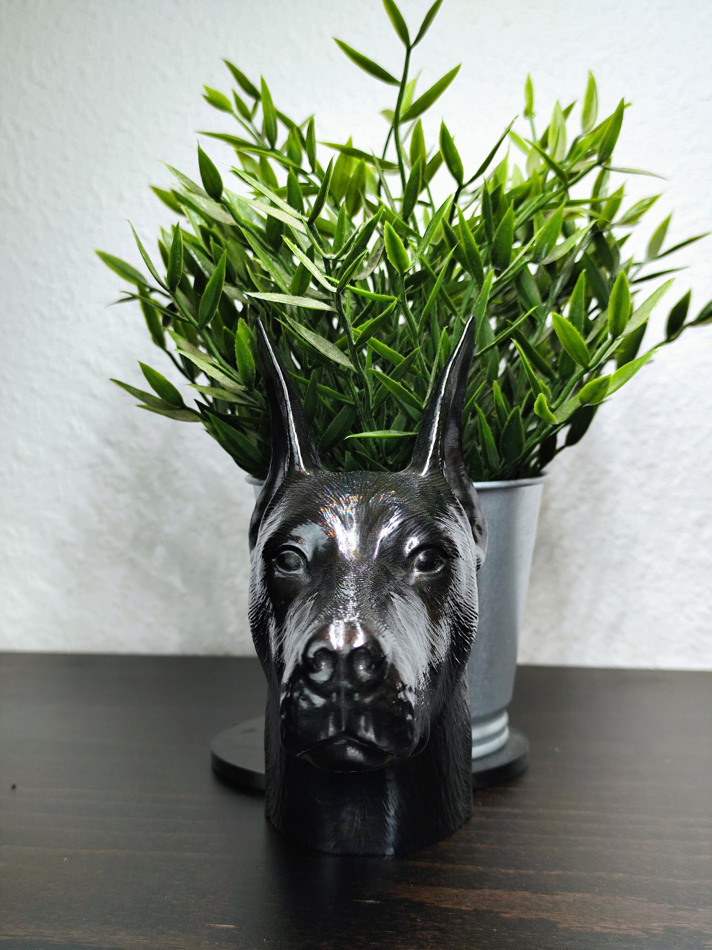 Close-up of a hand-painted Doberman planter featuring metallic gold and silver detailing, with a small green plant in the background. The planter captures the lifelike features of a Doberman&#39;s head with intricate details