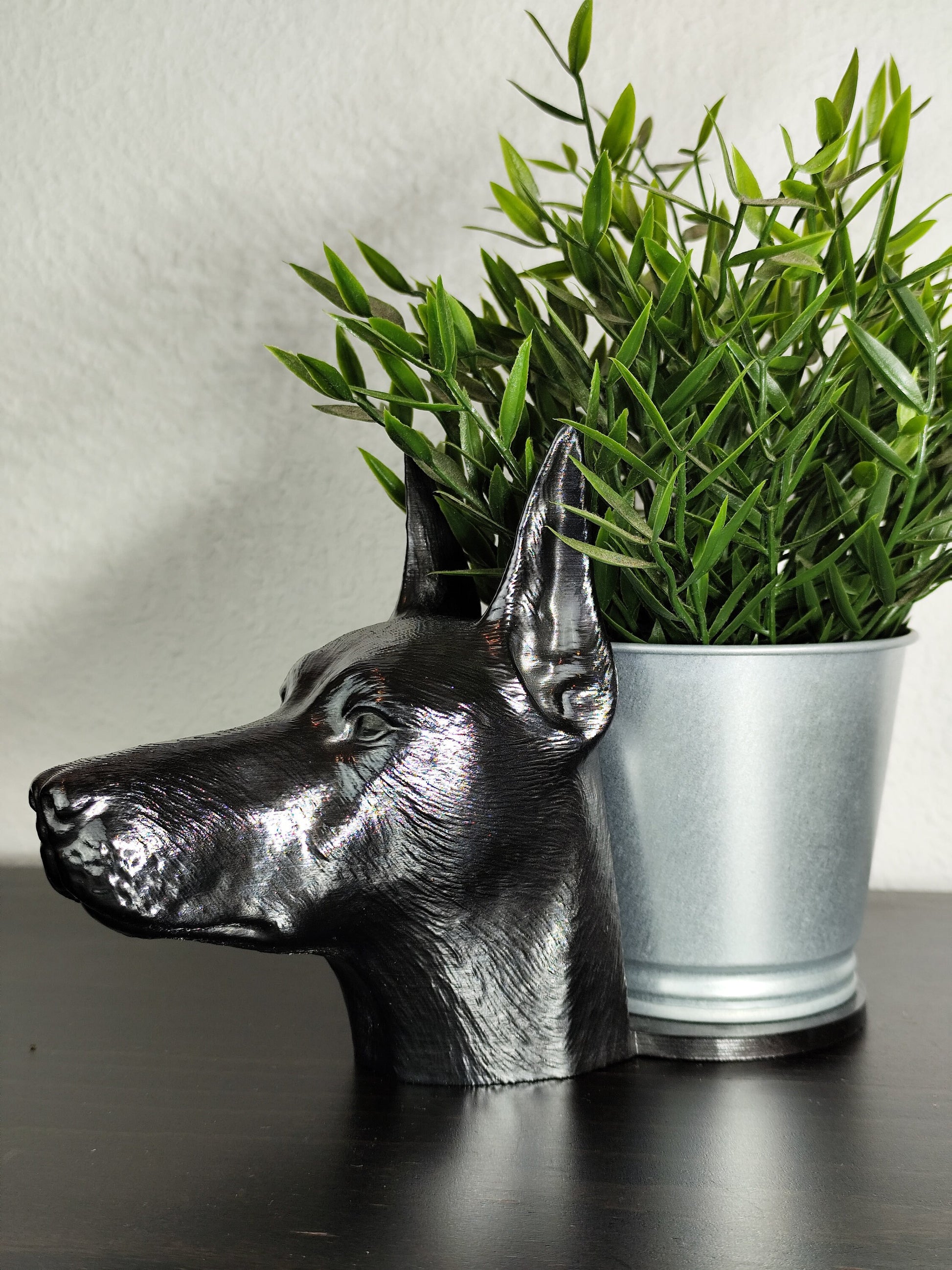 Close-up of a hand-painted Doberman planter featuring metallic gold and silver detailing, with a small green plant in the background. The planter captures the lifelike features of a Doberman&#39;s head with intricate details